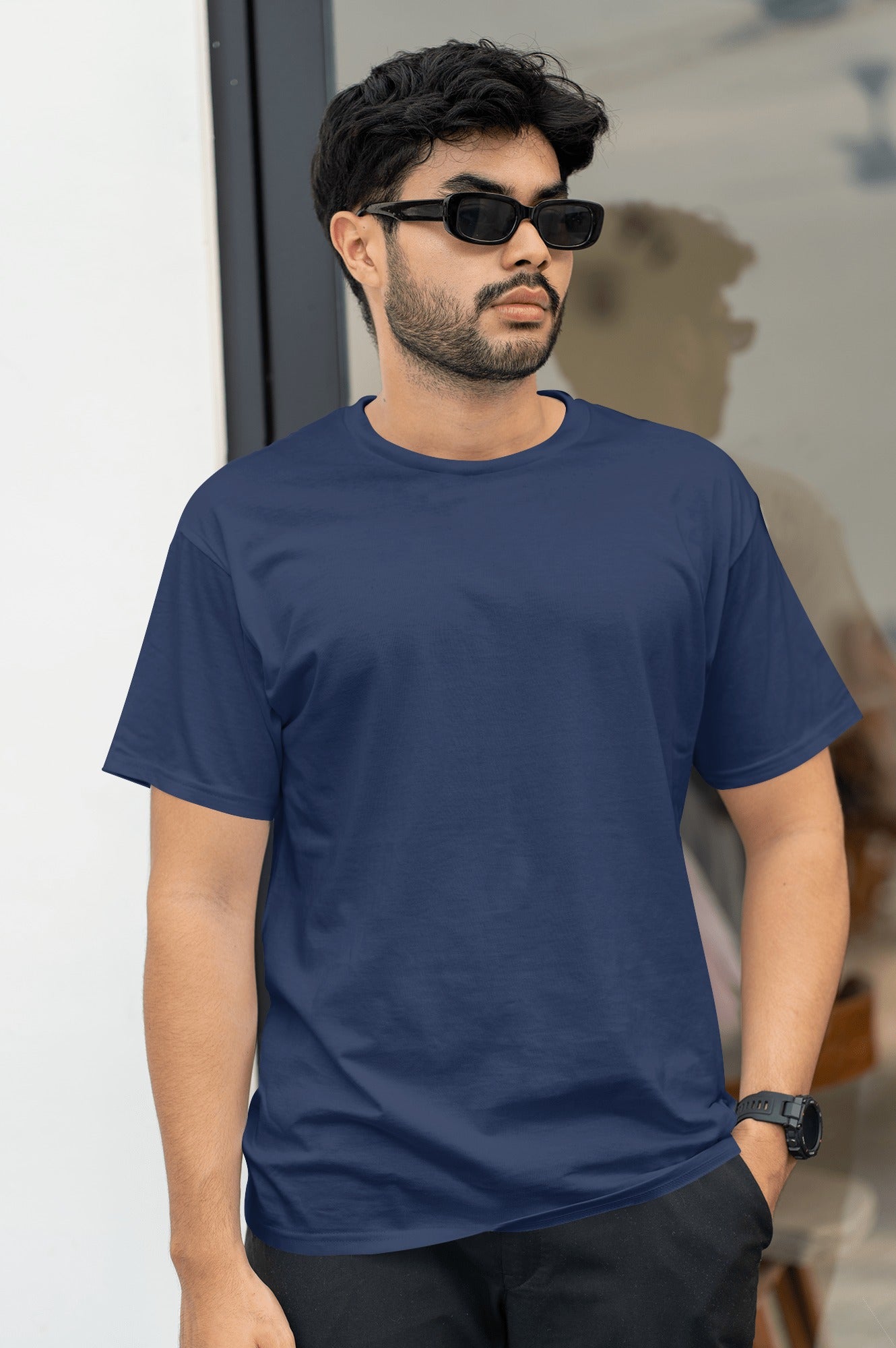 A man dressed in an blue t-shirt and sunglasses poses outdoors, radiating a relaxed summer vibe.