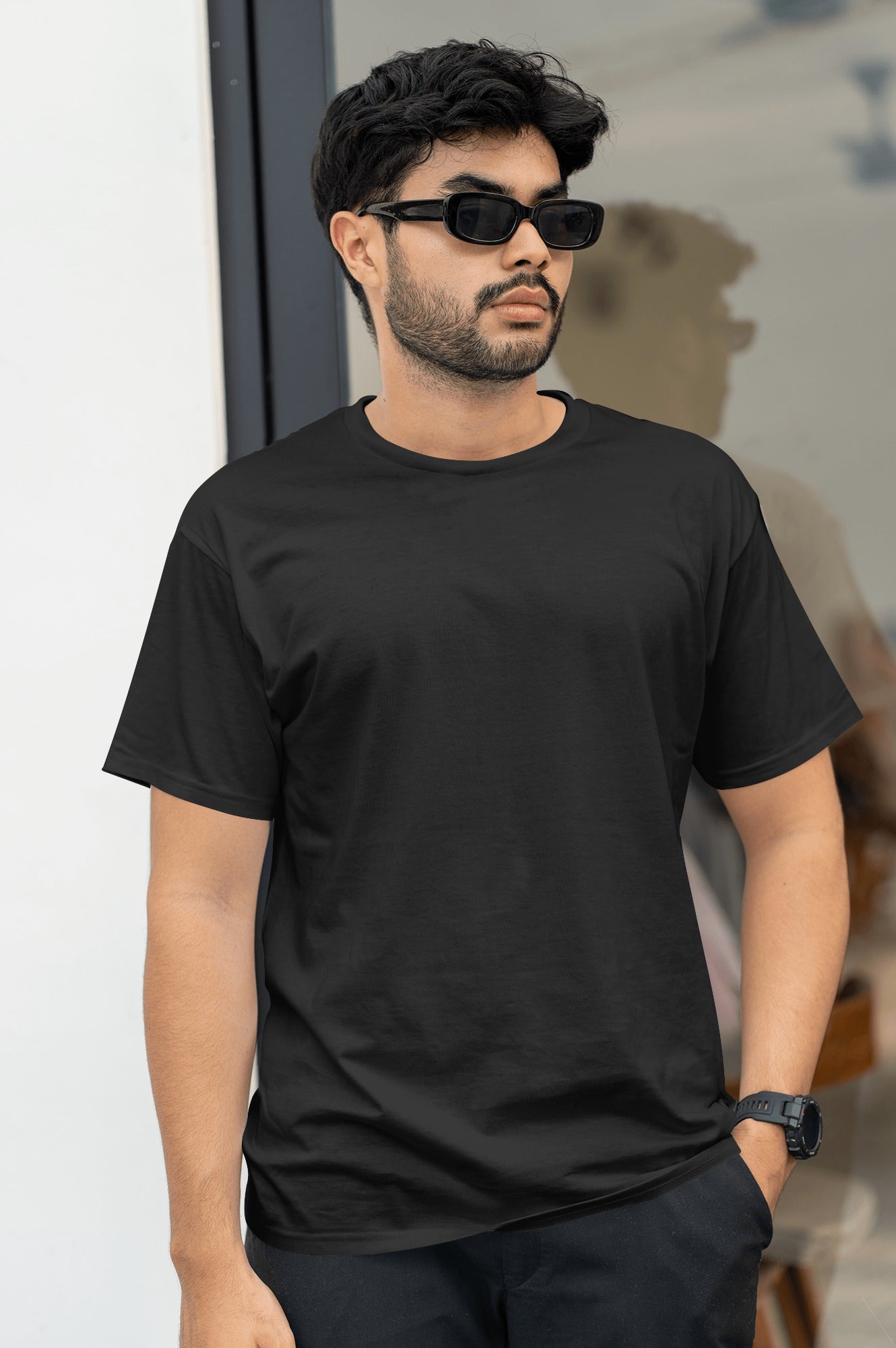 A man wearing sunglasses and an black t-shirt smiles while standing outside in bright sunlight.