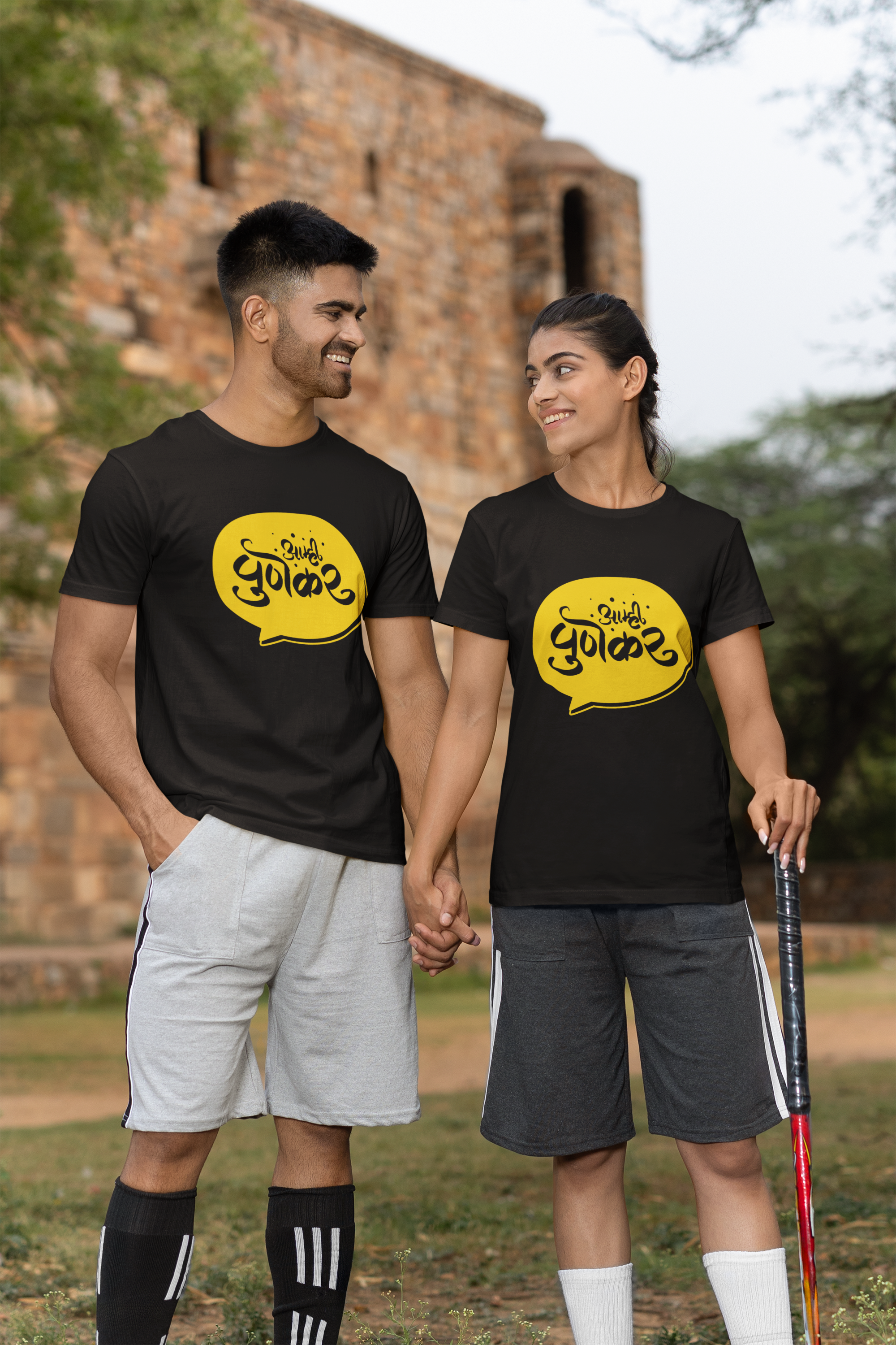 A couple in black t-shirts holding hands, smiling at each other in a casual outdoor setting.