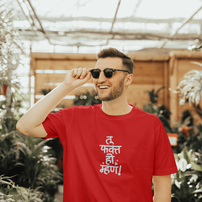 A man in sunglasses and a red t-shirt that says "tu fakt ho mhan," looking relaxed and cheerful outdoors.