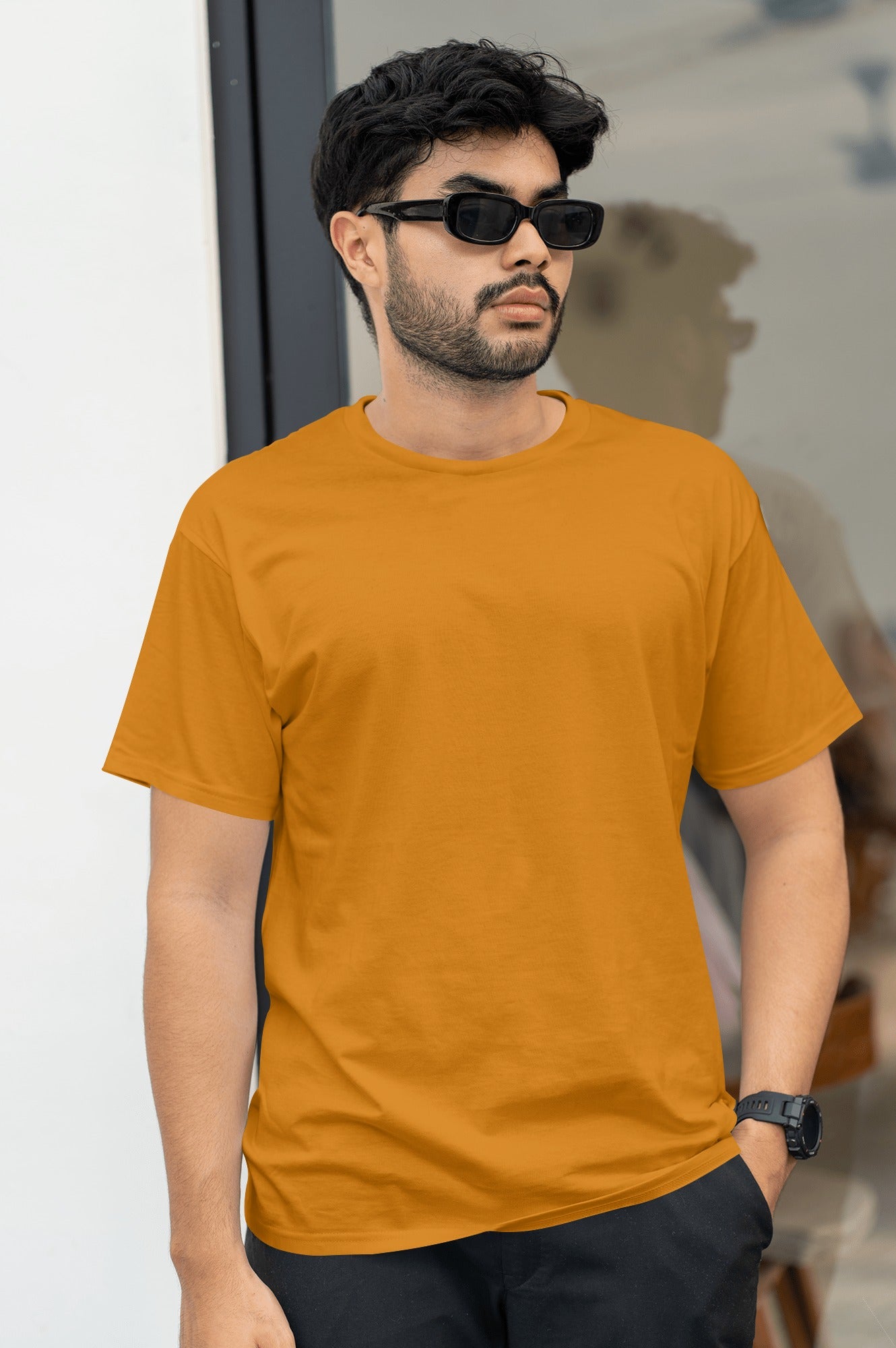 A man in an orange t-shirt and sunglasses stands confidently, enjoying a sunny day outdoors.